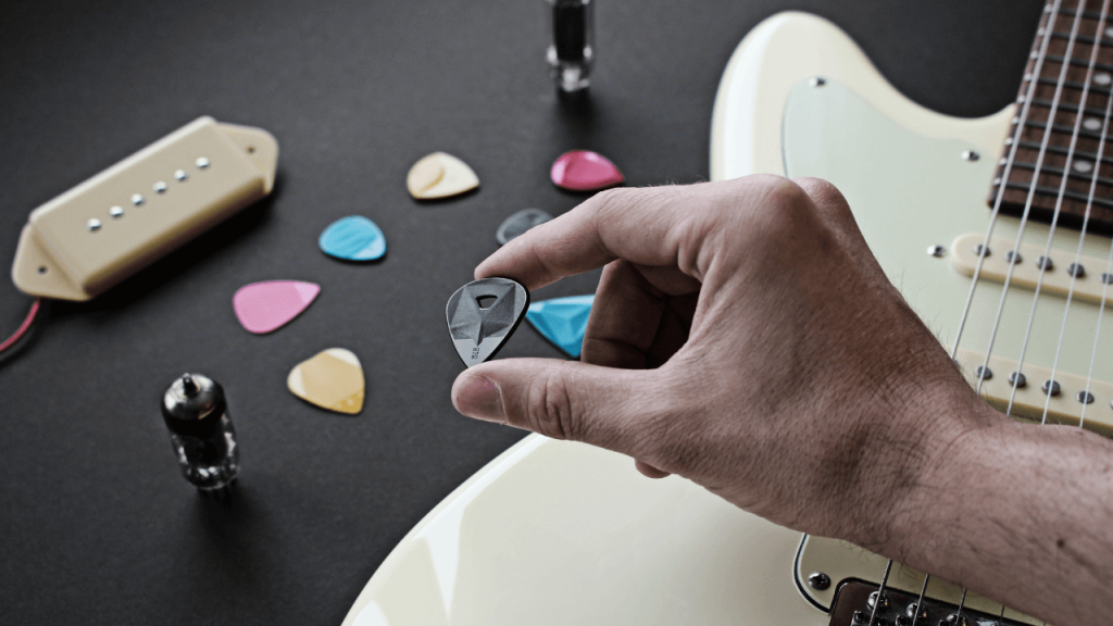 A person holding a black guitar pick with various other types of picks in the background